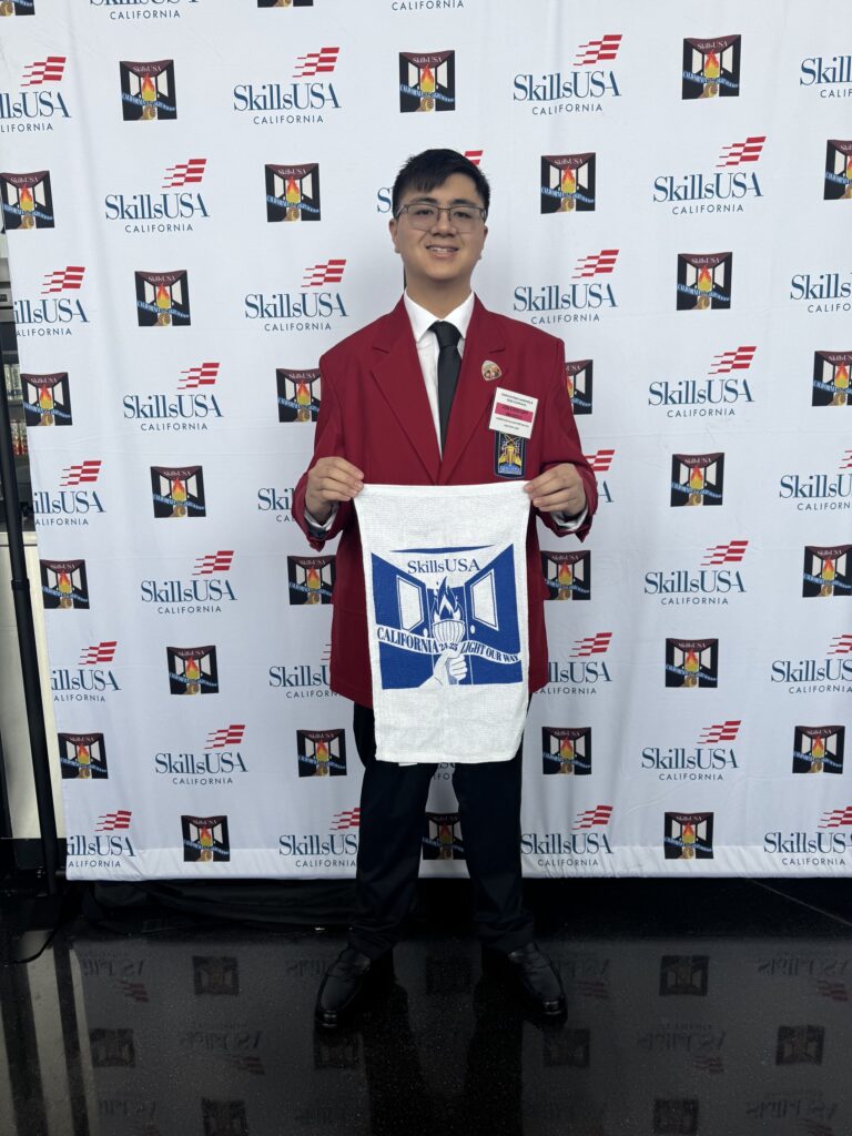 JC في معرض «SkillsUSA California» وهو يرفع لافتة زرقاء وبيضاء.