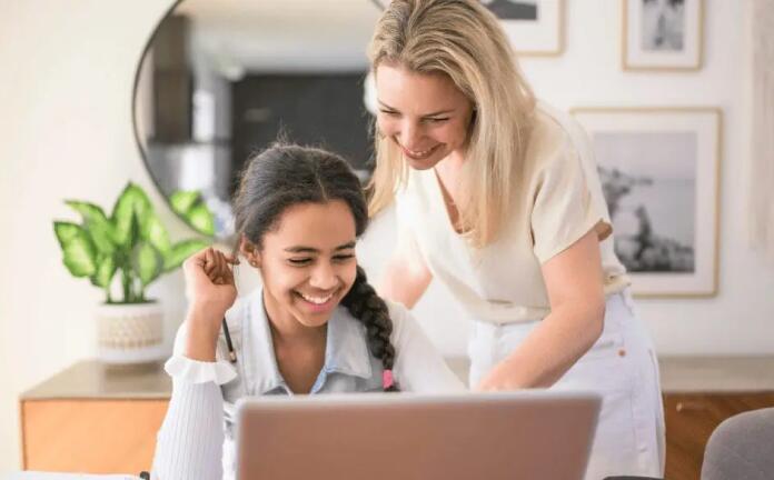 أم وابنتها تعملان معًا على جهاز الكمبيوتر المحمول في المنزل